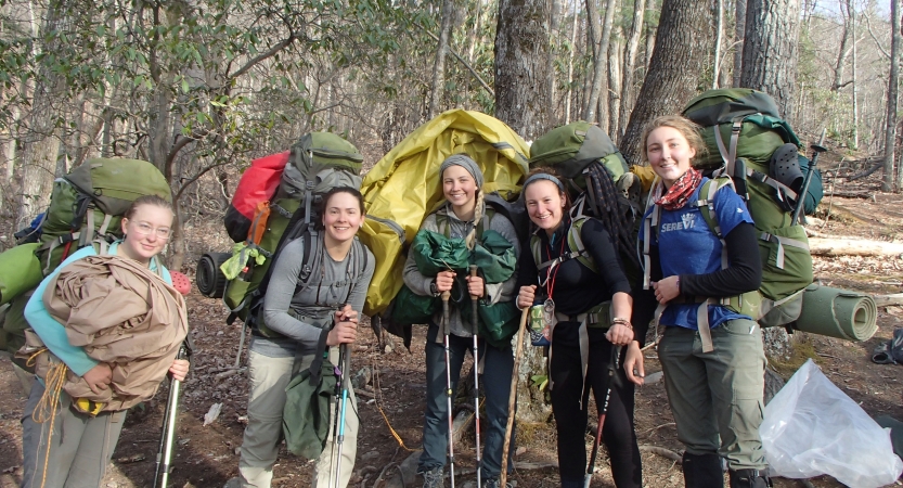 a group of people wearing backpacks pose for a photo in a wooded area